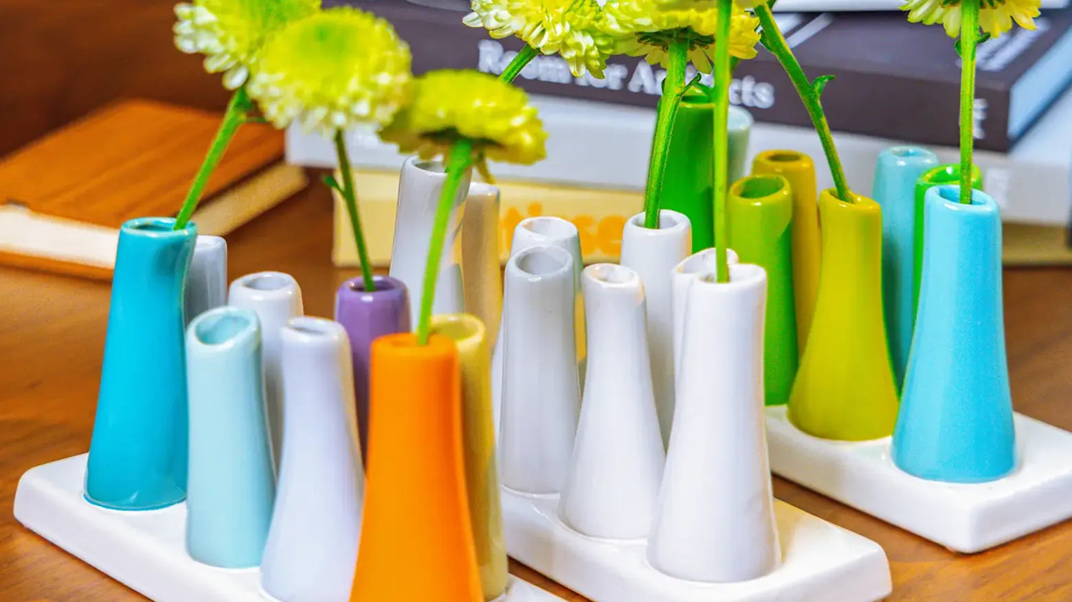 Chive ceramic pooley bud vase in color white, orange, and scout blue styled with fresh flowers, on a wood desk.