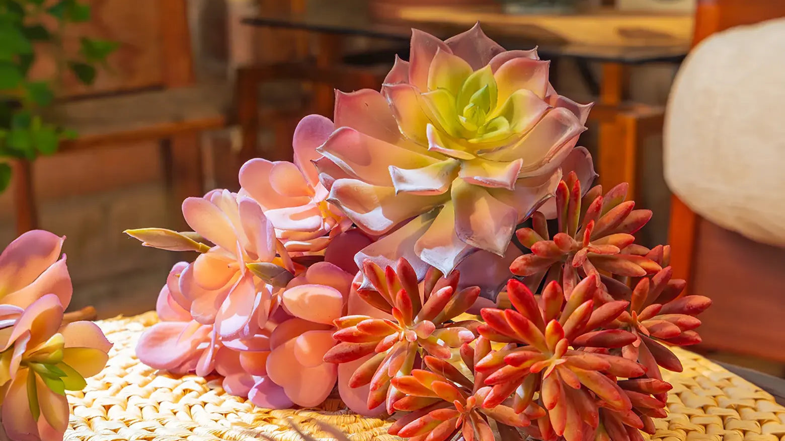 Chive realistic pink-yellow faux succulent echeveria stems arranged on a woven round mat on a wood table — with lifelike color gradients and leaf textures