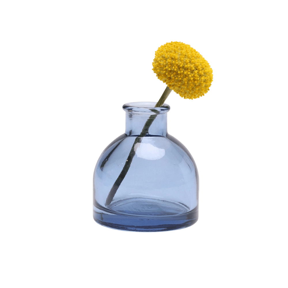 Chive Loft round glass bud vase in medium blue, shown from a side angle with a yellow billy ball bloom.