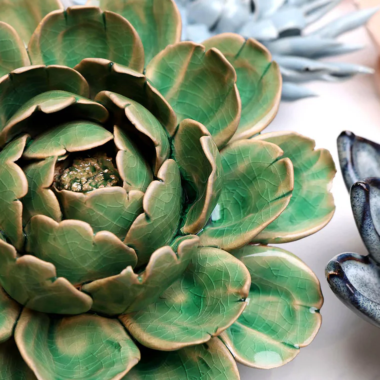 Close-up of a green ceramic succulent plant with other decorative plants in the background.