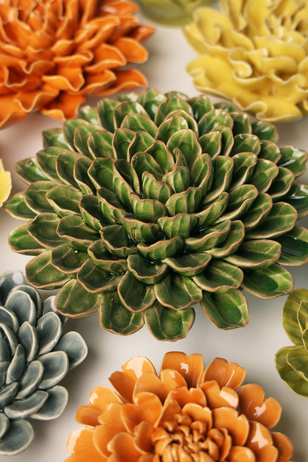 Avocado Green Zinnia ceramic wall flower styled on a white table with other flowers — Chive Studio