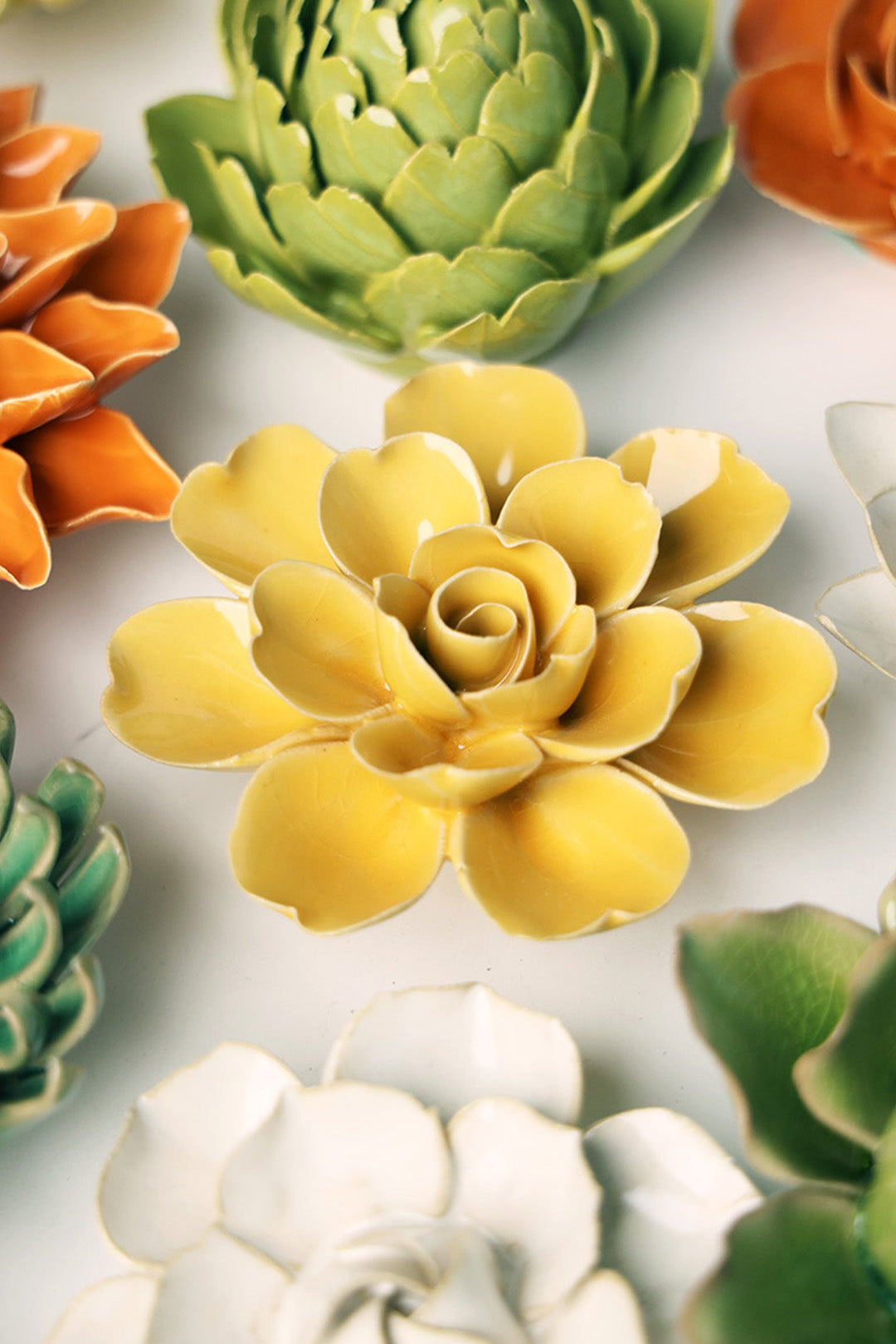 Burnt Yellow Gardenia ceramic wall flower styled on a white table with other flowers — Chive Studio