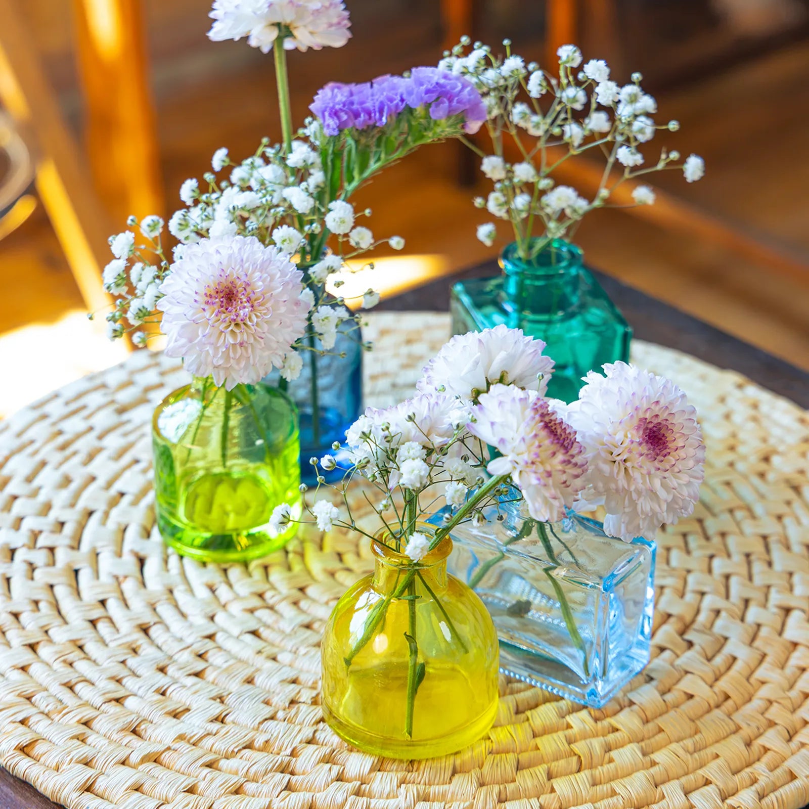 Chive Loft glass bud vase set in assorted shapes and colors on a table mat, each styled with flowers.