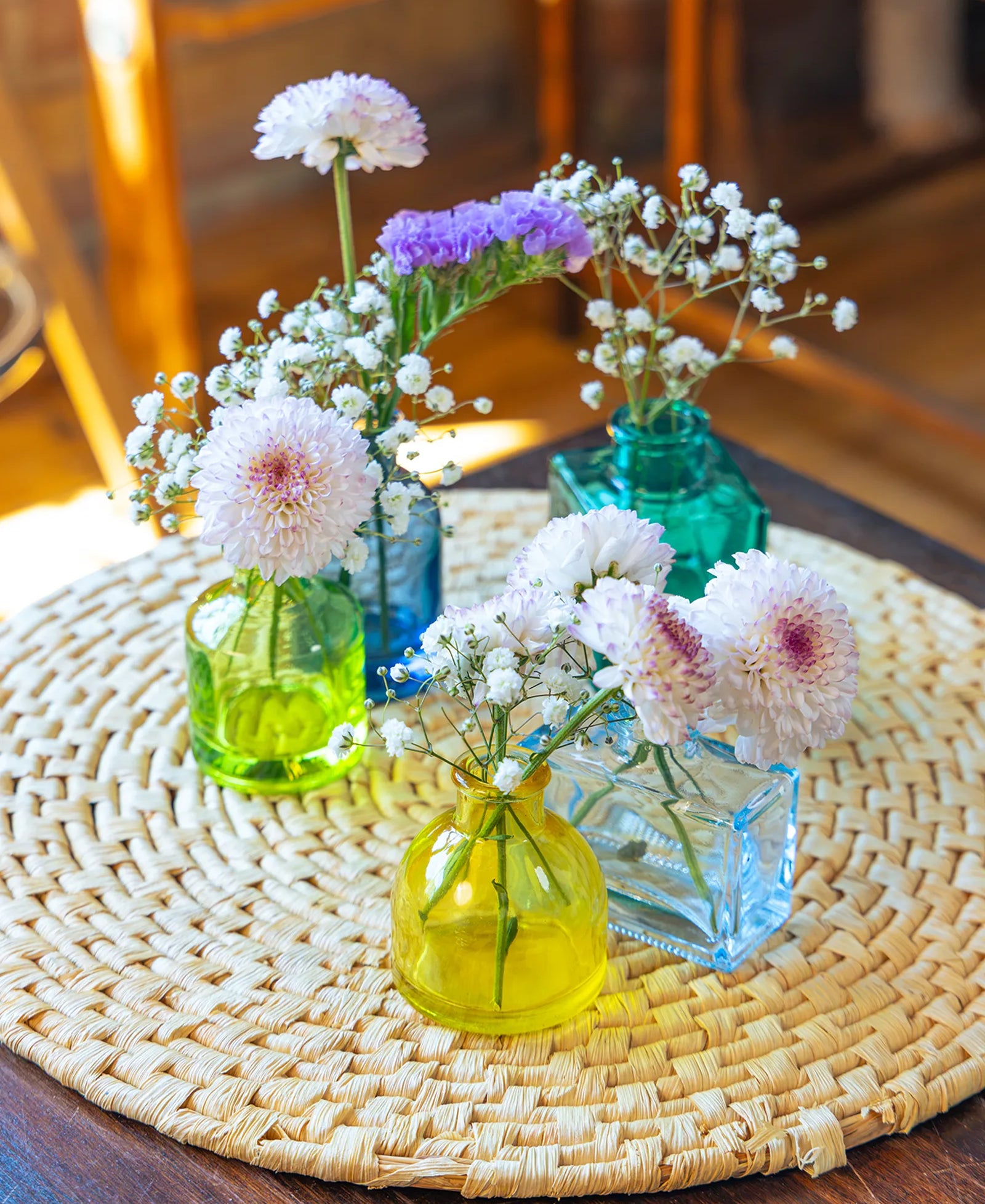 Chive Loft glass bud vase set in assorted shapes and colors on a table mat, each styled with flowers.