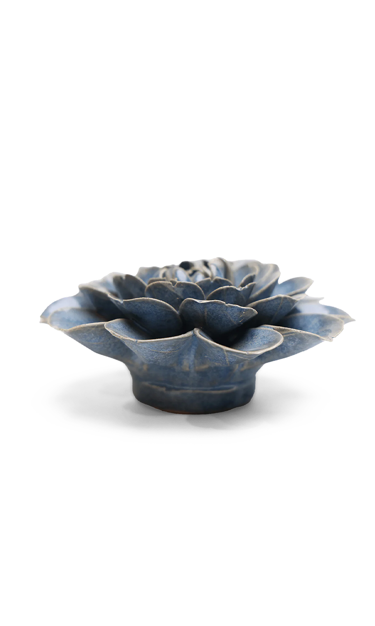 A small sculptural flower-shaped object with layered petals, shown on a clean white background. The item has a glossy dark blue glaze with lighter blue-gray highlights and a slightly distressed, rustic finish.