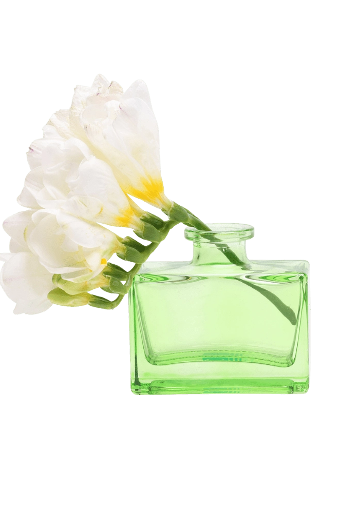 Chive Loft square glass bud vase in green holding freesia blooms, shown from a side angle.