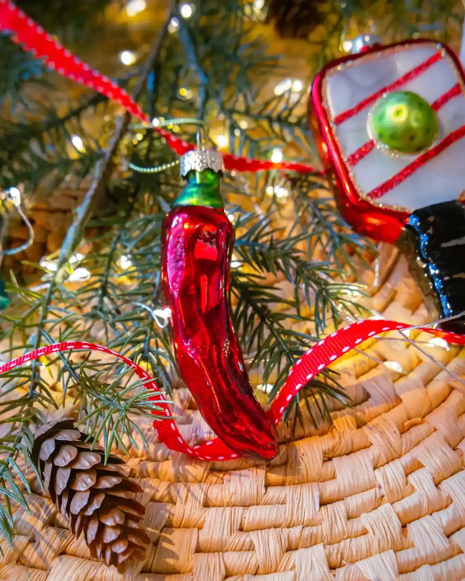 Chive glass chili pepper ornament in red hanging on a holiday tree.