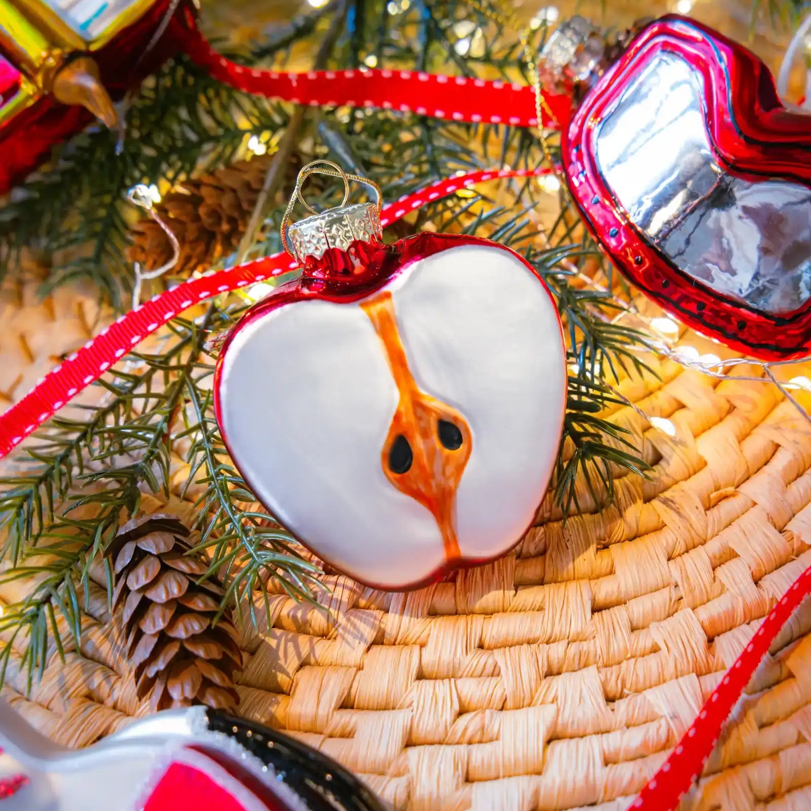 Chive glass sliced apple ornament in red hanging on a holiday tree.