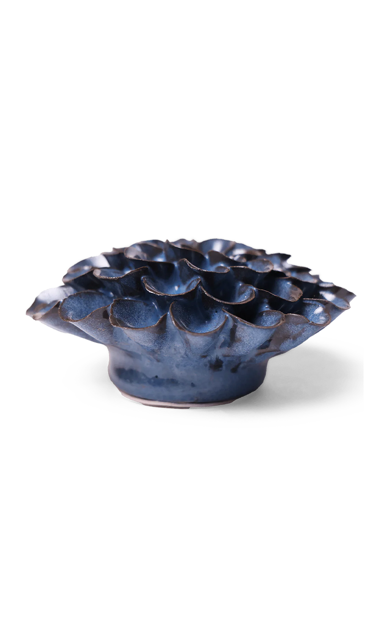 A small sculptural ceramic vessel with a ruffled, lotus-like top and a rounded base, shown on a clean white background. The glaze is predominantly deep blue with dark brown and black variation along the edges and highlights.