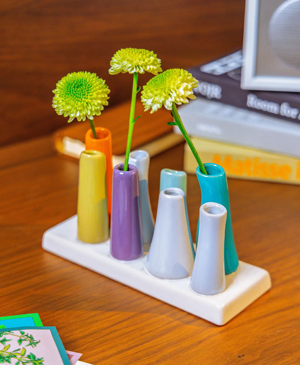 Chive ceramic pooley bud vase in color orange, styled with fresh flowers, on a wood desk.