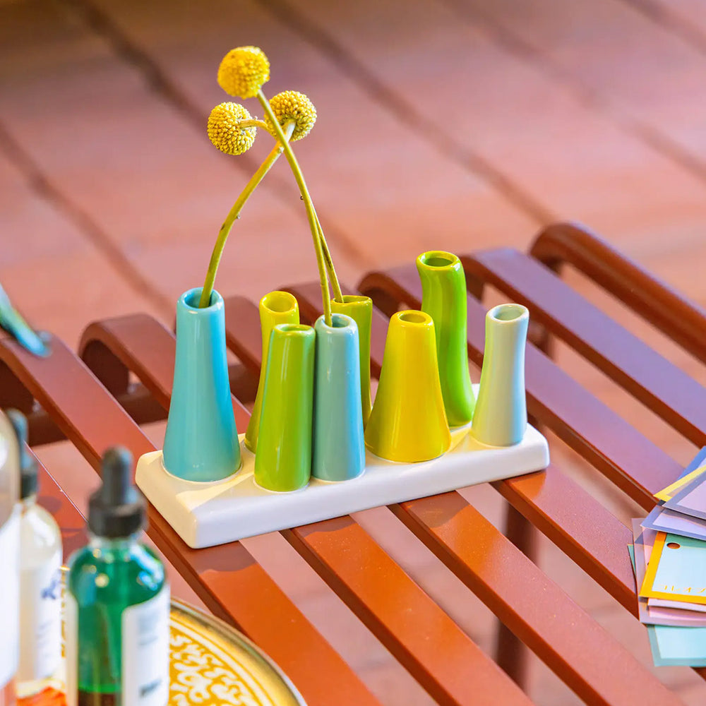 Chive ceramic pooley bud vase in color scout blue, styled with fresh flowers, on a red bench.