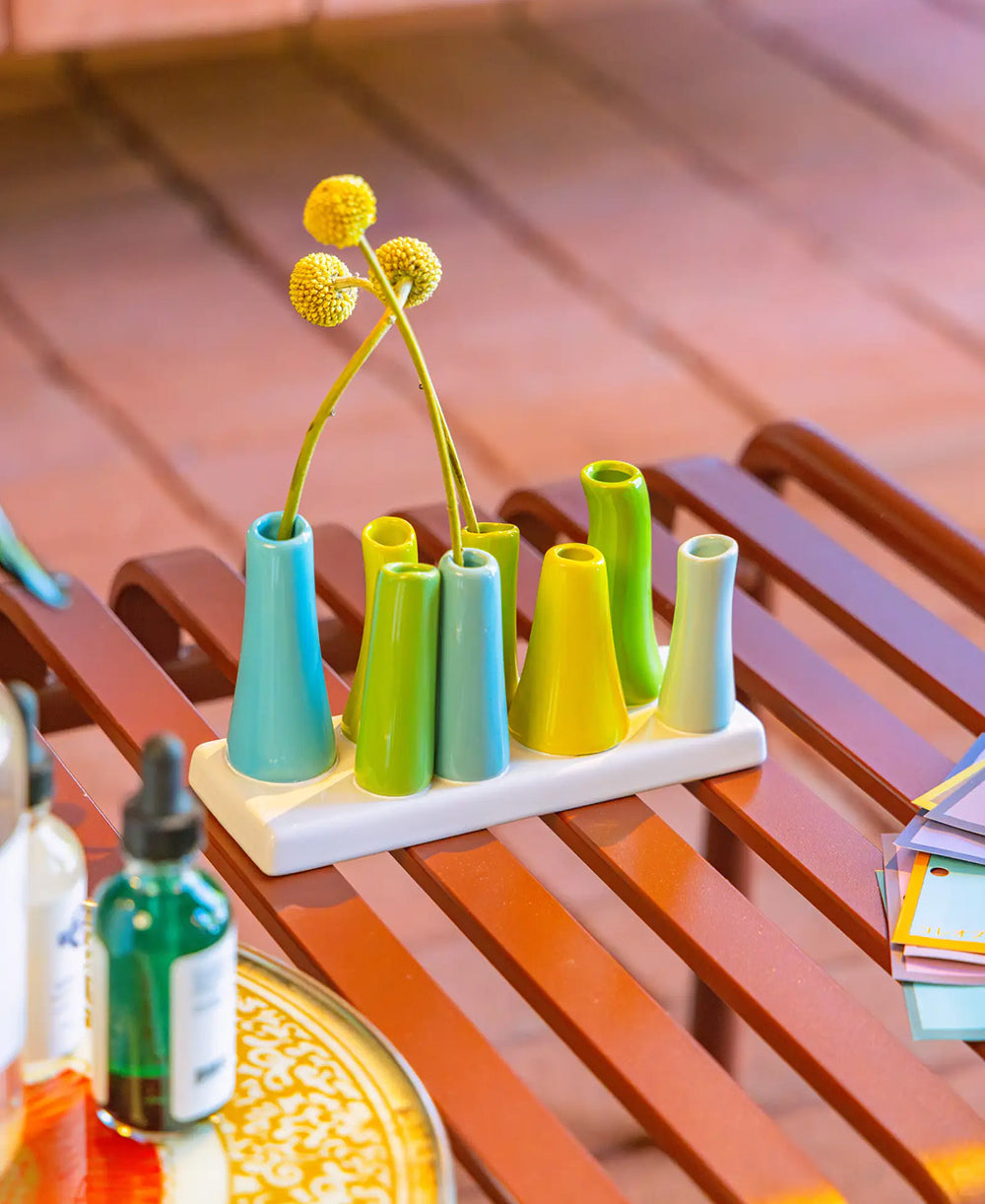 Chive ceramic pooley bud vase in color scout blue, styled with fresh flowers, on a red bench.