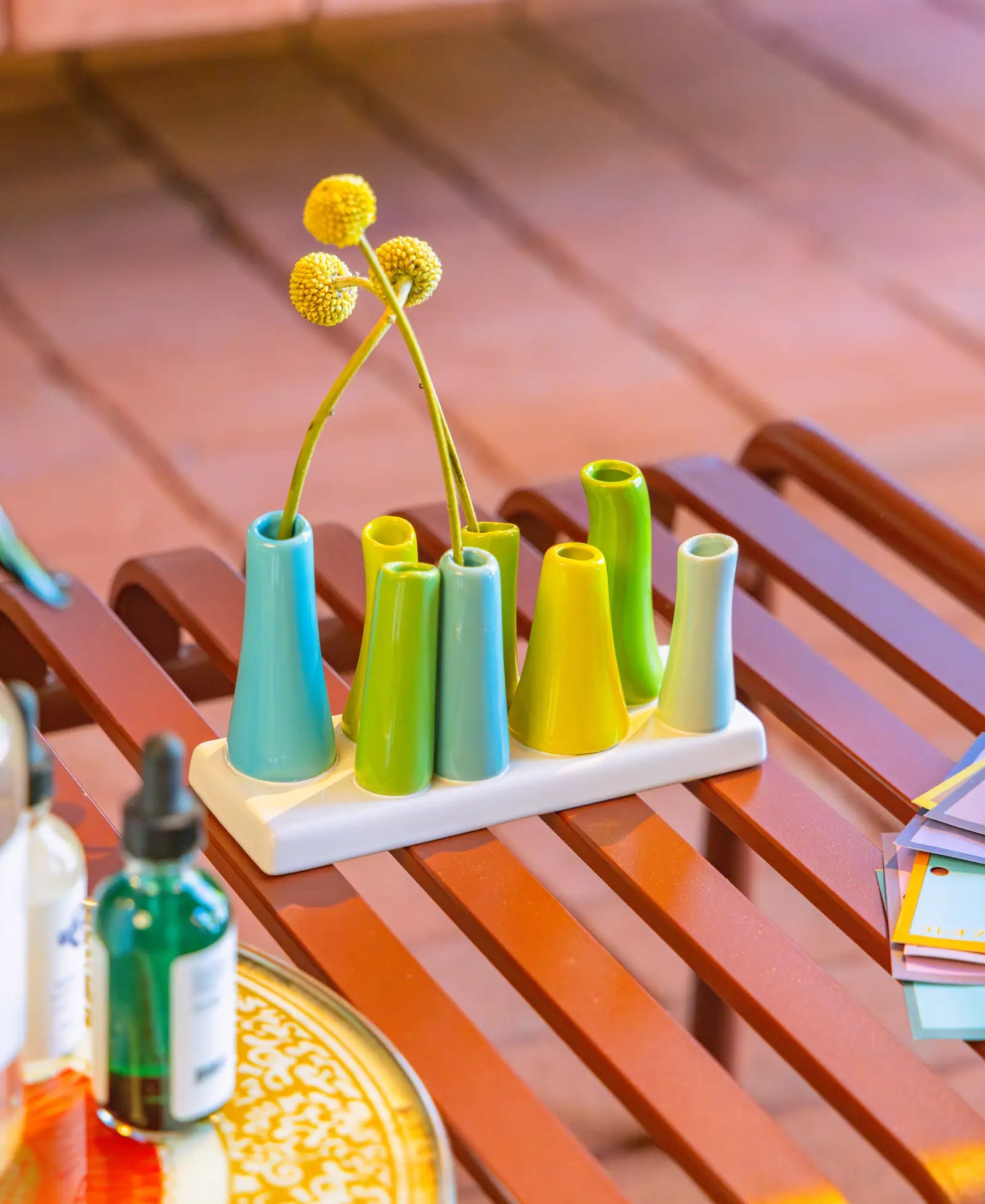 Chive ceramic pooley bud vase in color scout blue, styled with fresh flowers, on a red bench.