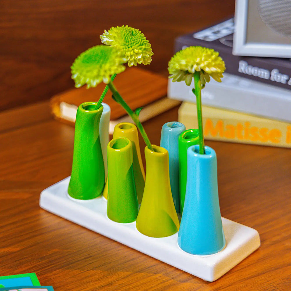 Chive ceramic pooley bud vase in color scout blue, styled with fresh flowers, on a wood desk.