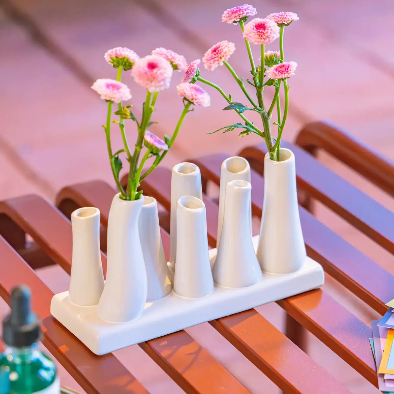 Chive ceramic pooley bud vase in white, styled with fresh pink flowers, on a red bench.