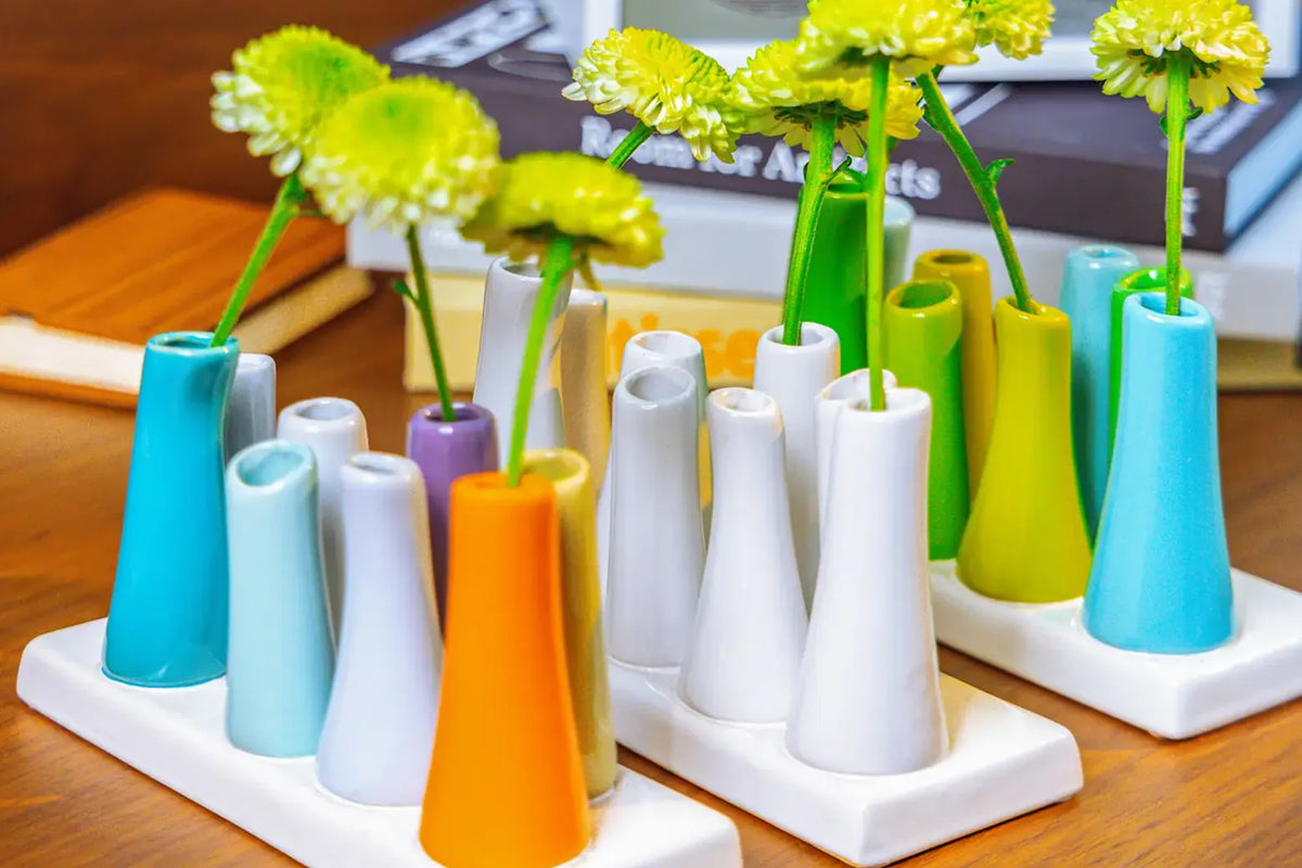 Chive ceramic pooley bud vase in color white, orange, and scout blue styled with fresh flowers, on a wood desk.