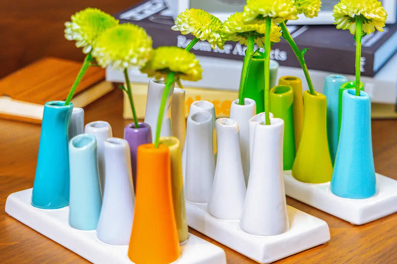 Chive ceramic pooley bud vase in color white, orange, and scout blue styled with fresh flowers, on a wood desk.