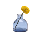 Chive Loft round glass bud vase in medium blue, shown from a side angle with a yellow billy ball bloom.