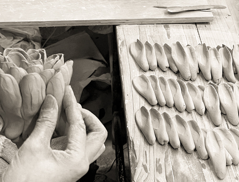 Chive Studio artisan sculpting a ceramic flower by hand attaching clay petals on a wood slab workbench — handmade without molds since 1999