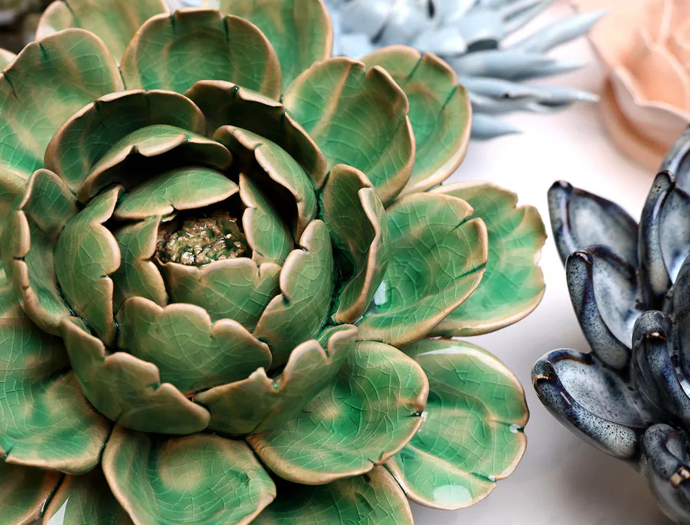 Close-up of a green ceramic succulent plant with other decorative plants in the background.