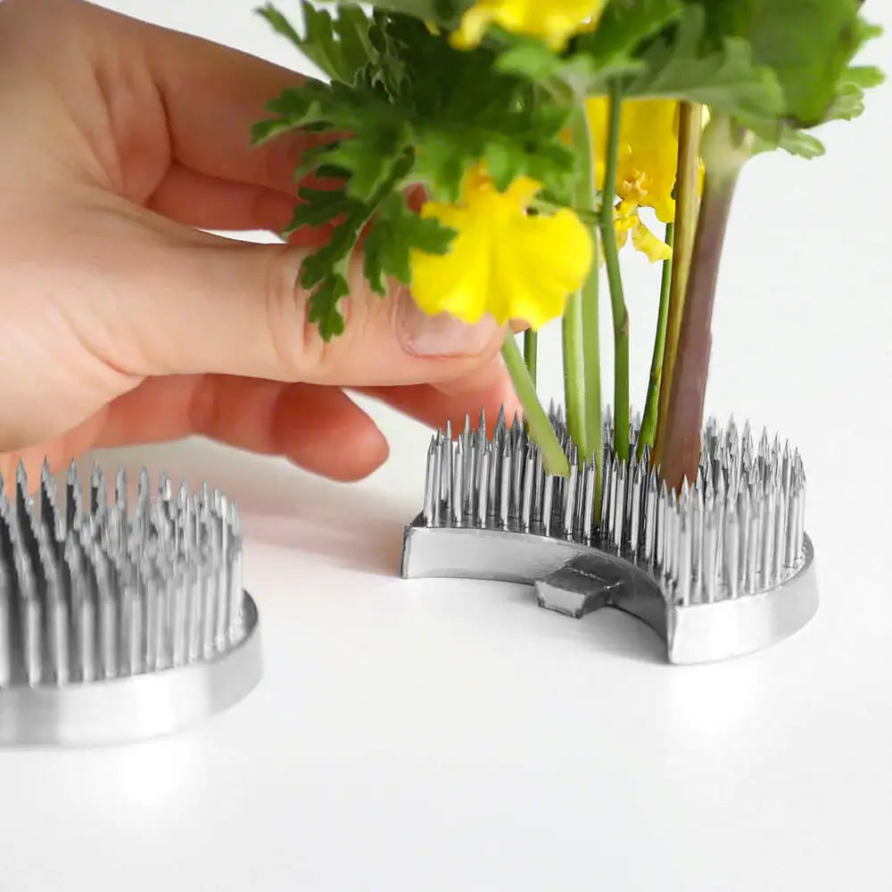 A person's hand pressing fresh flowers onto a metal flower frog.