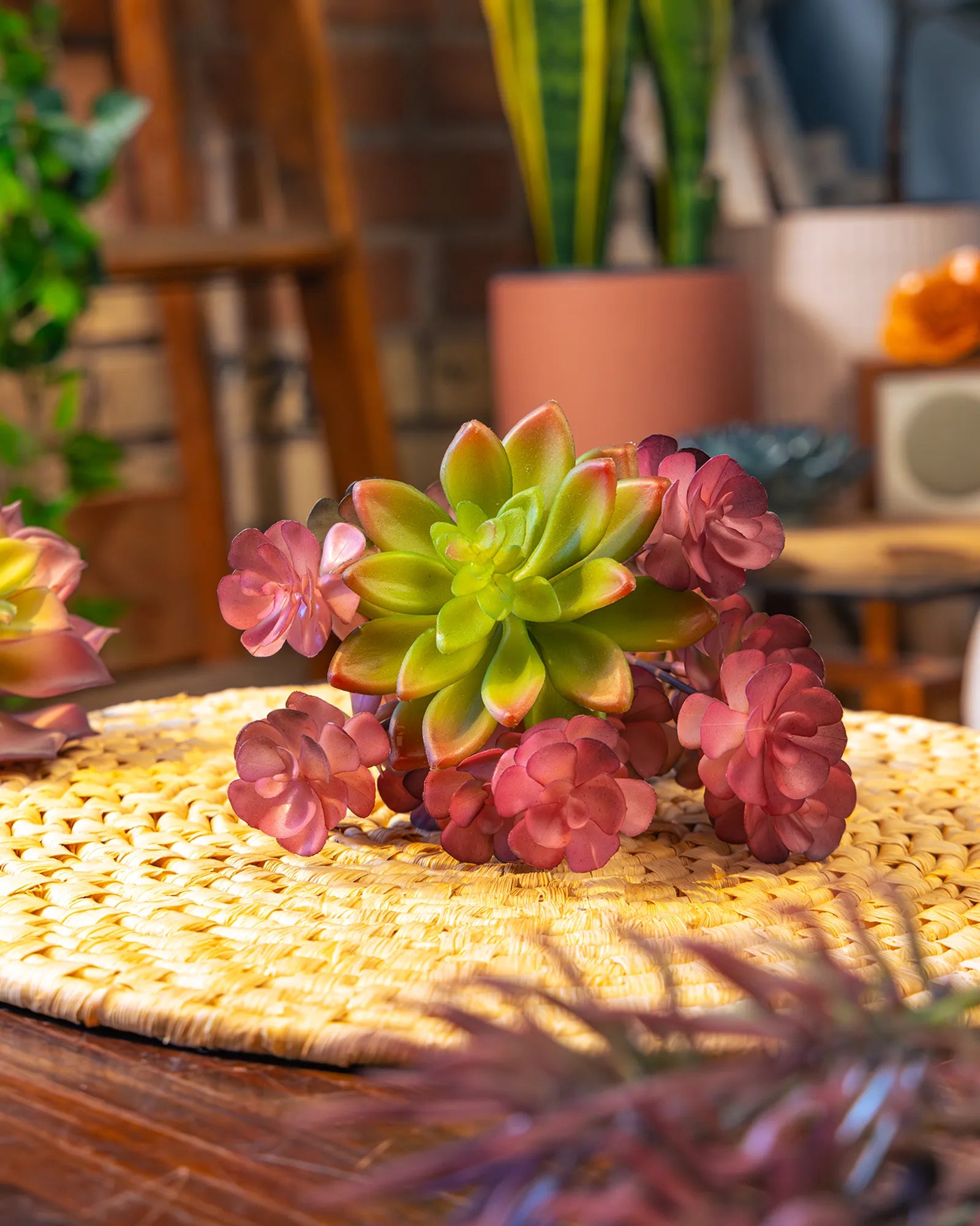 A cluster of Chive realistic green-red faux succulent echeveria stems arranged on a woven round mat on a wood table.