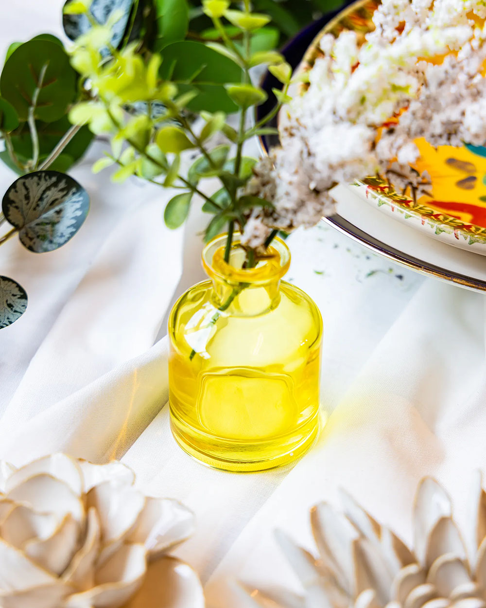 Close up of a wedding tabletop arrangement with a Chive Loft yellow glass bud vases holding white flowers.