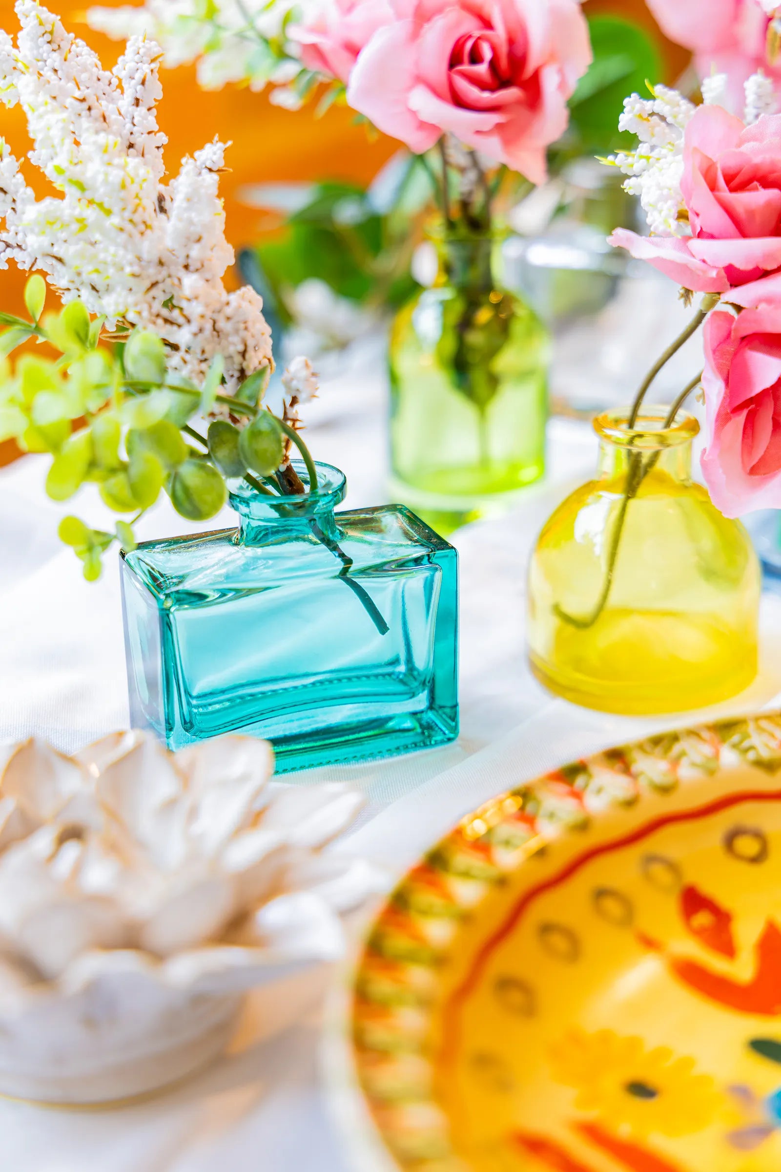 Close up of a wedding tabletop arrangement with three Chive Loft glass bud vases in teal, green, and yellow holding pink and white flowers.