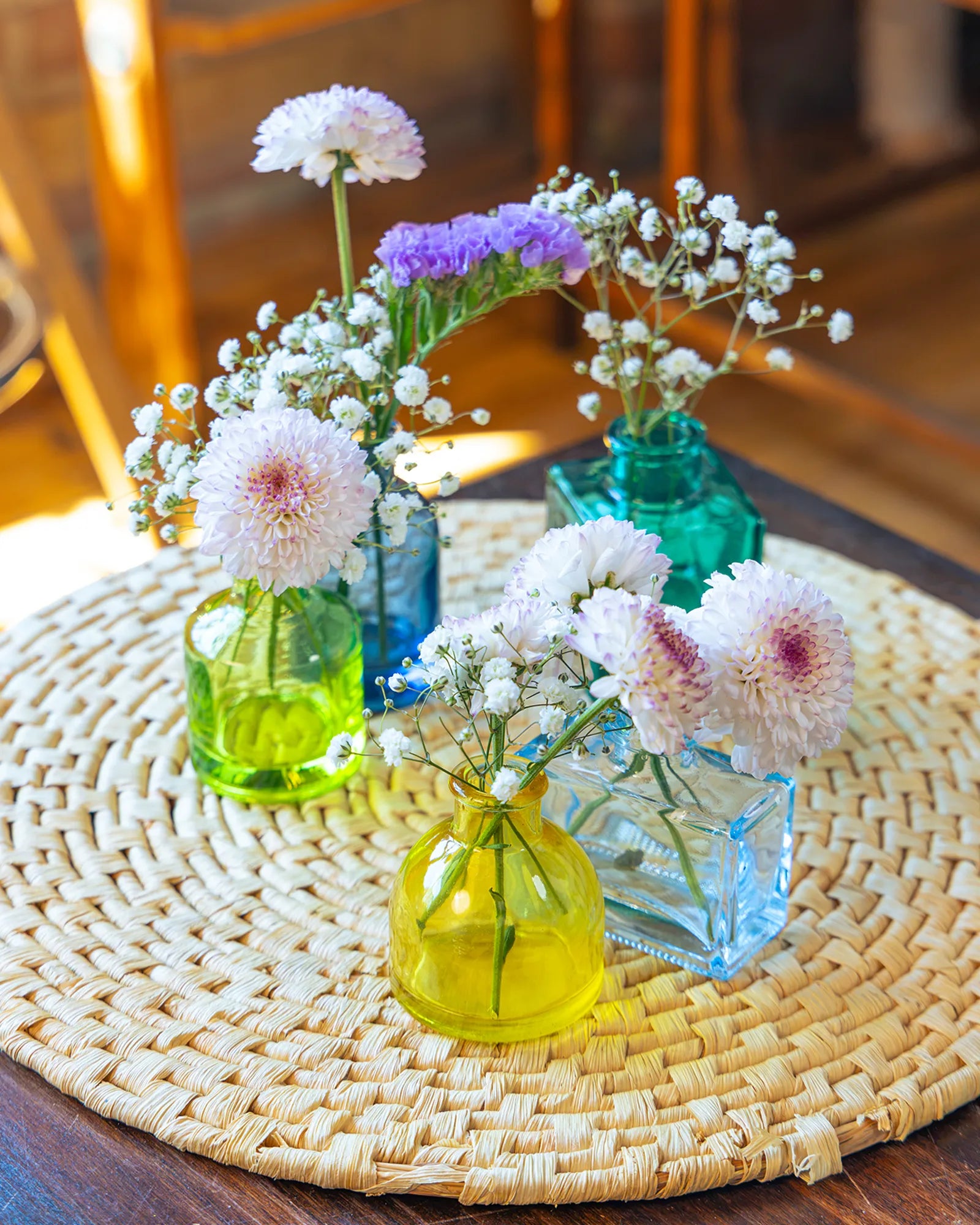Chive Loft glass bud vase set in assorted shapes and colors on a table mat, each styled with flowers.
