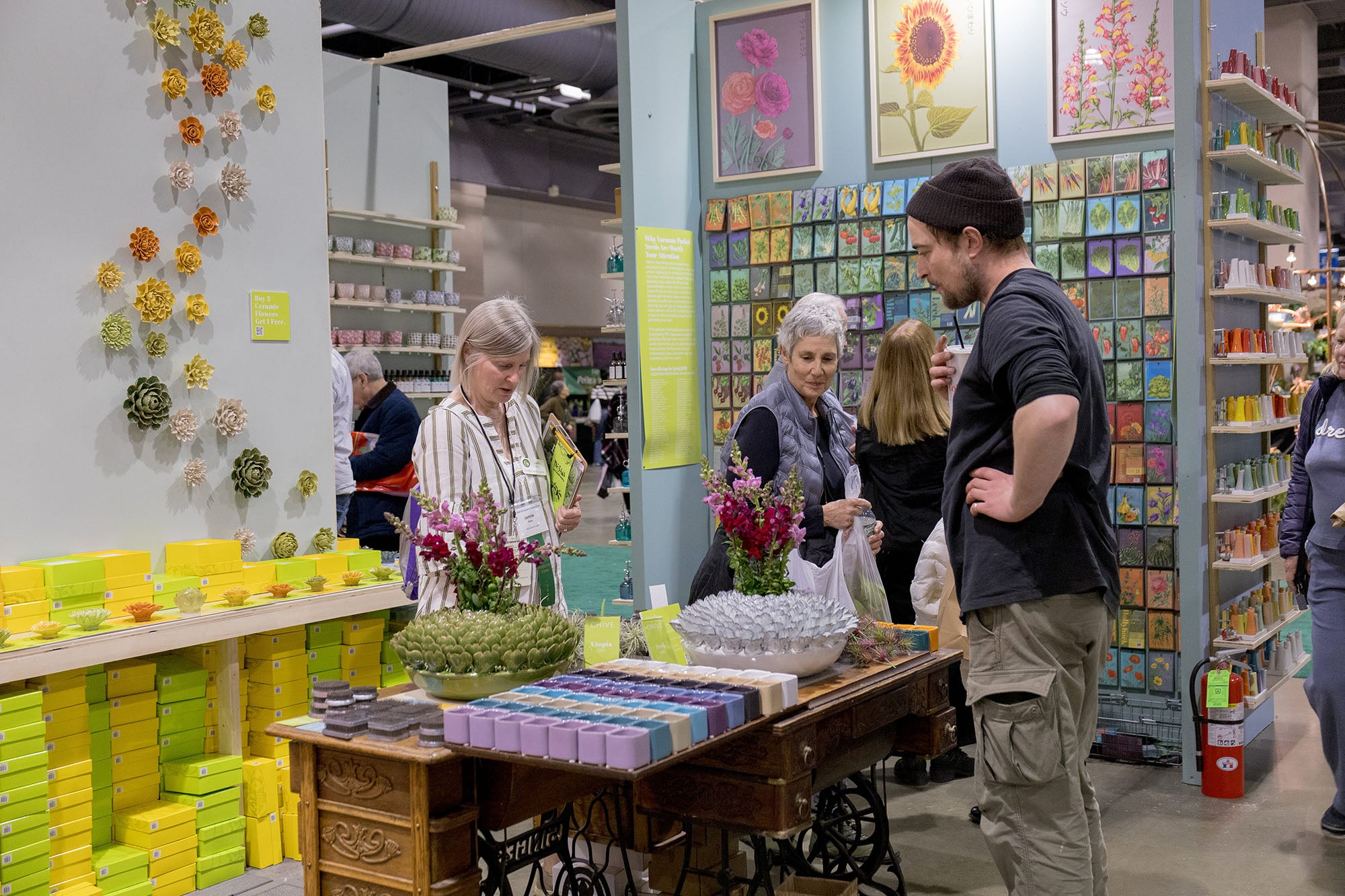 Chive Studio employee speaking with customers at Philadelphia Flower Show booth with ceramic wall flowers displayed in an S shape and Shido Seeds packets on wall — Chive Studio
