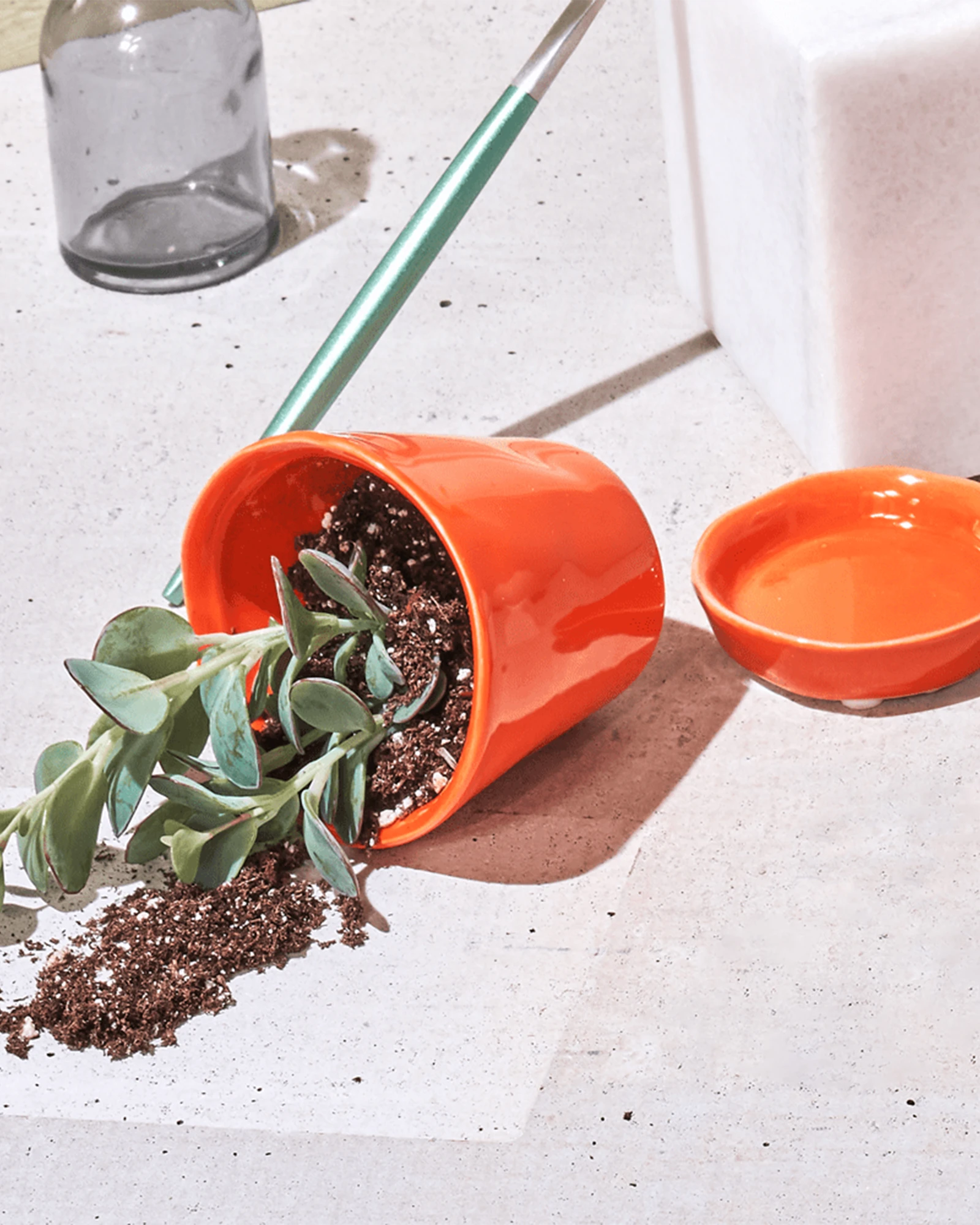 Chive Tika orange ceramic small planter tipped on its side with soil and a succulent spilling out on a stone surface.