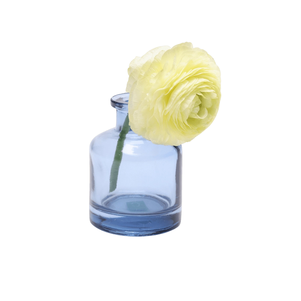 Chive Loft apothecary glass bud vase in medium blue, shown from a side angle with a yellow ranunculus.