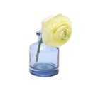 Chive Loft apothecary glass bud vase in medium blue, shown from a side angle with a yellow ranunculus.