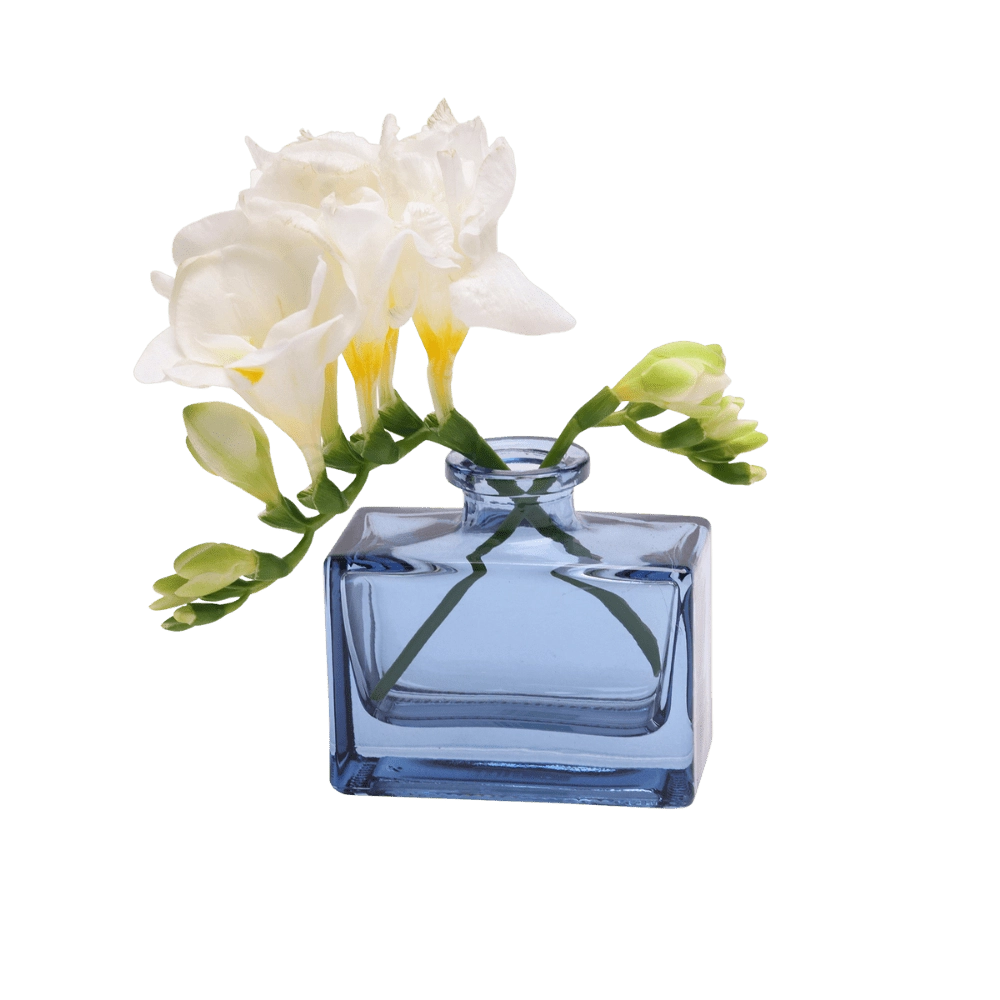 Chive Loft square glass bud vase in blue-grey holding freesia blooms, shown from a side angle.