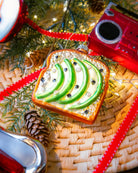 Chive glass avocado toast ornament in green hanging on a holiday tree.