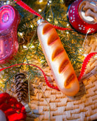 Chive glass baguette ornament in gold hanging on a holiday tree.