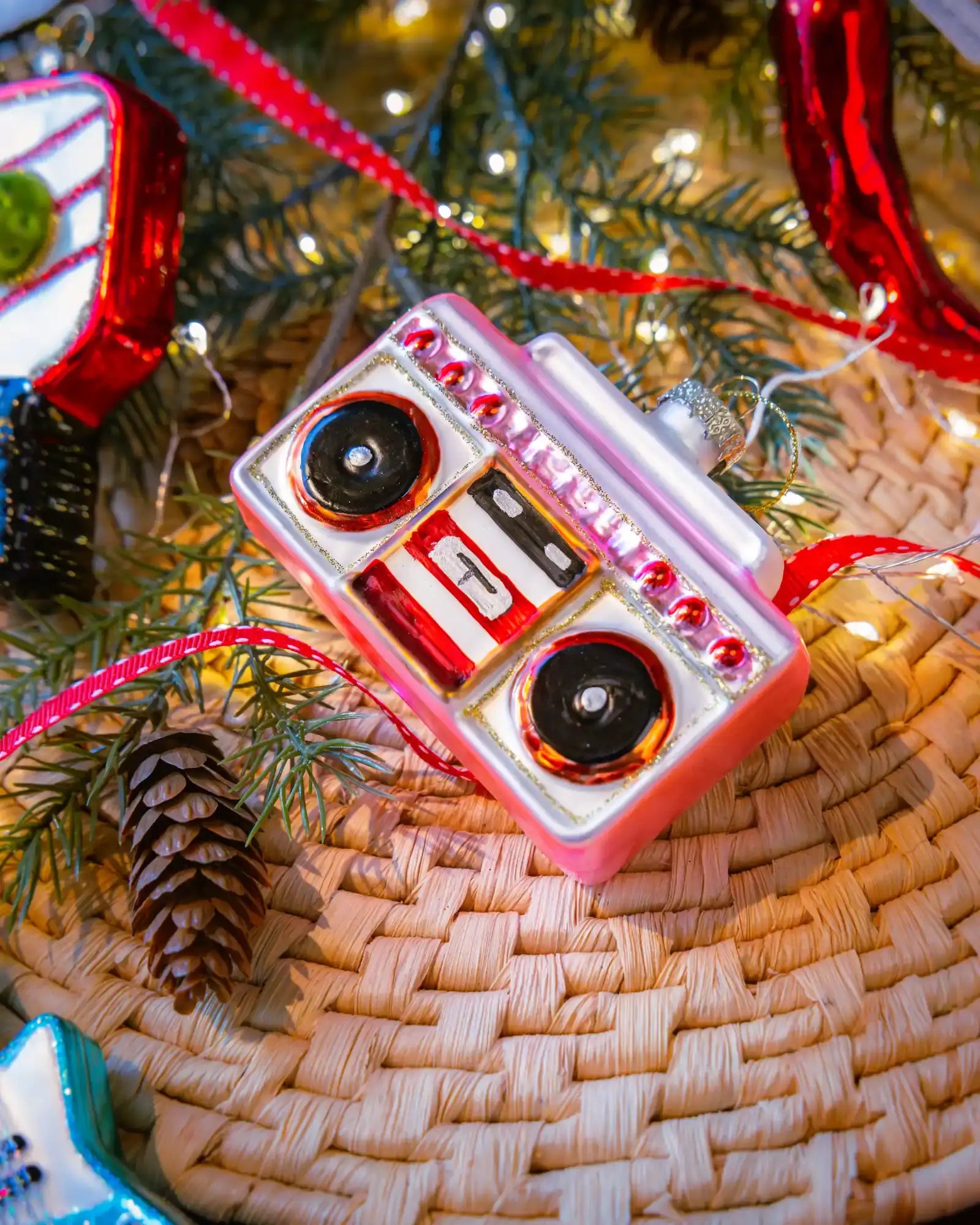 Chive glass boombox ornament in pink hanging on a holiday tree.