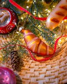 Chive glass croissant ornament in gold hanging on a holiday tree.