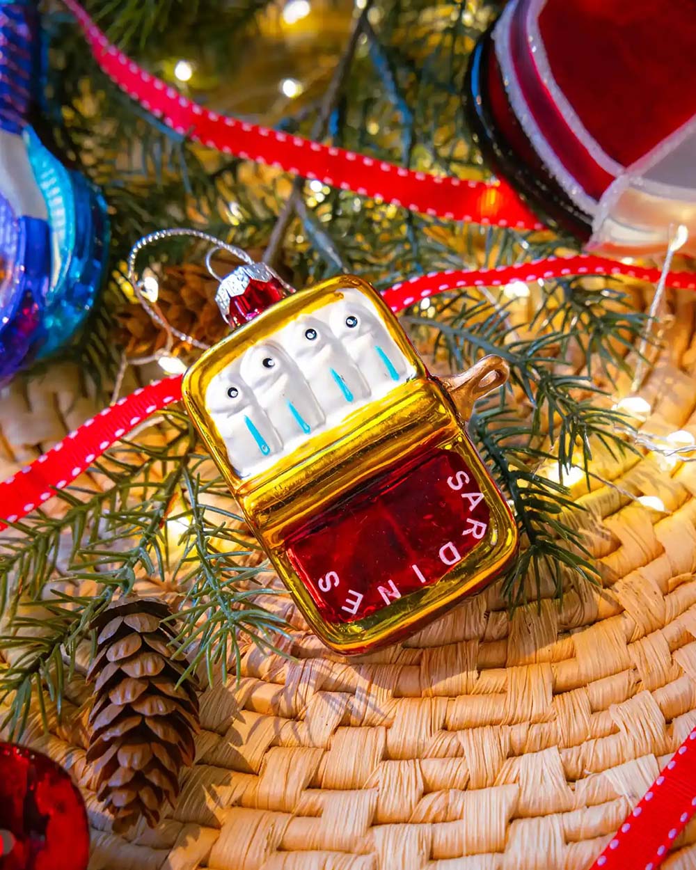 Chive glass sardine can ornament in red and gold hanging on a holiday tree.