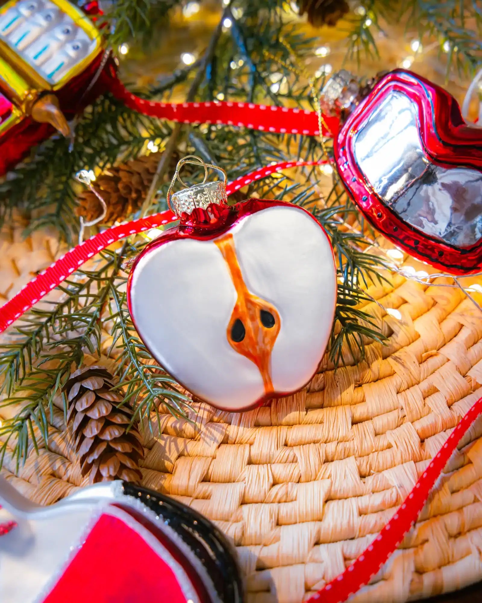 Chive glass sliced apple ornament in red hanging on a holiday tree.