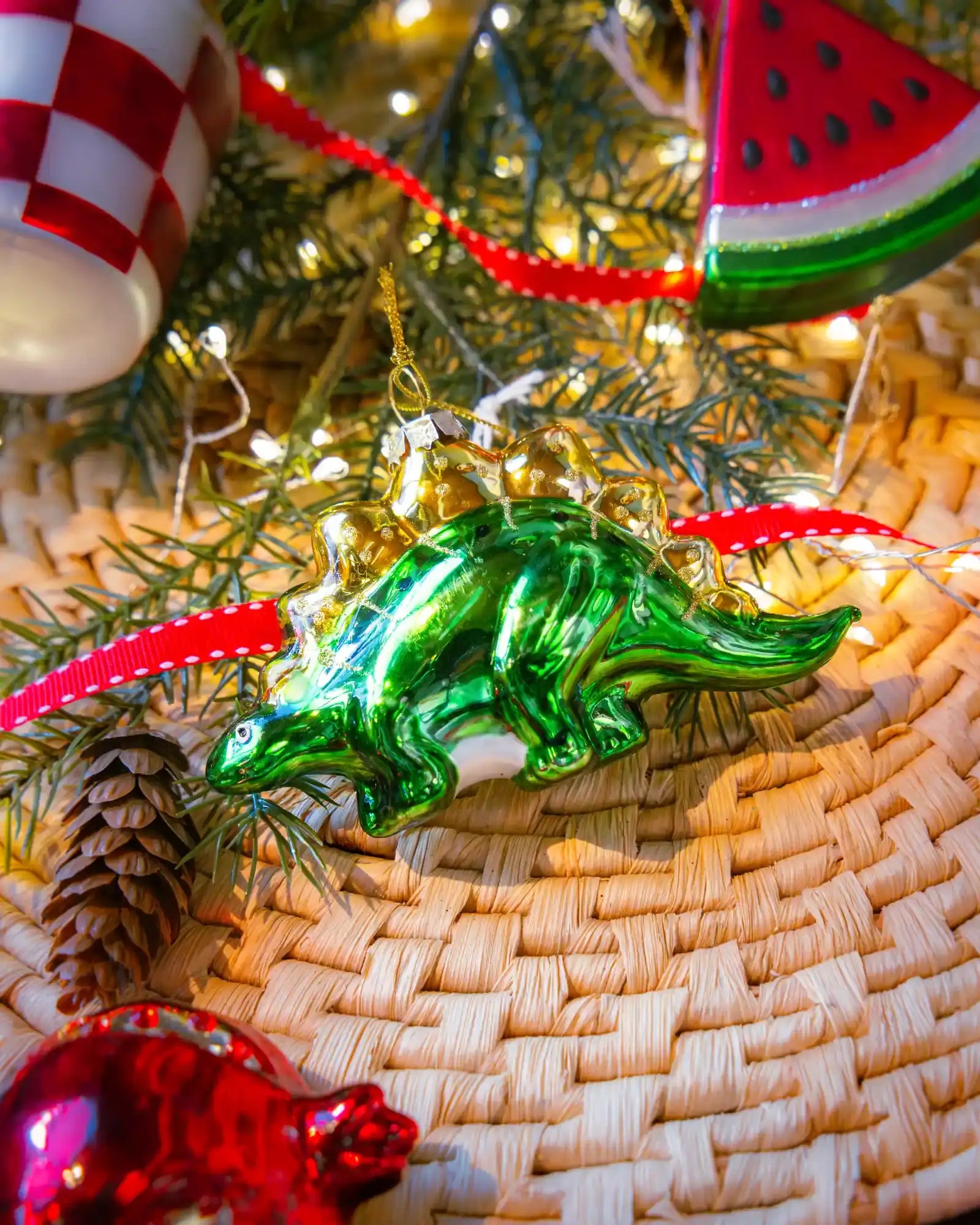 Chive glass stegosaurus ornament in green hanging on a holiday tree.