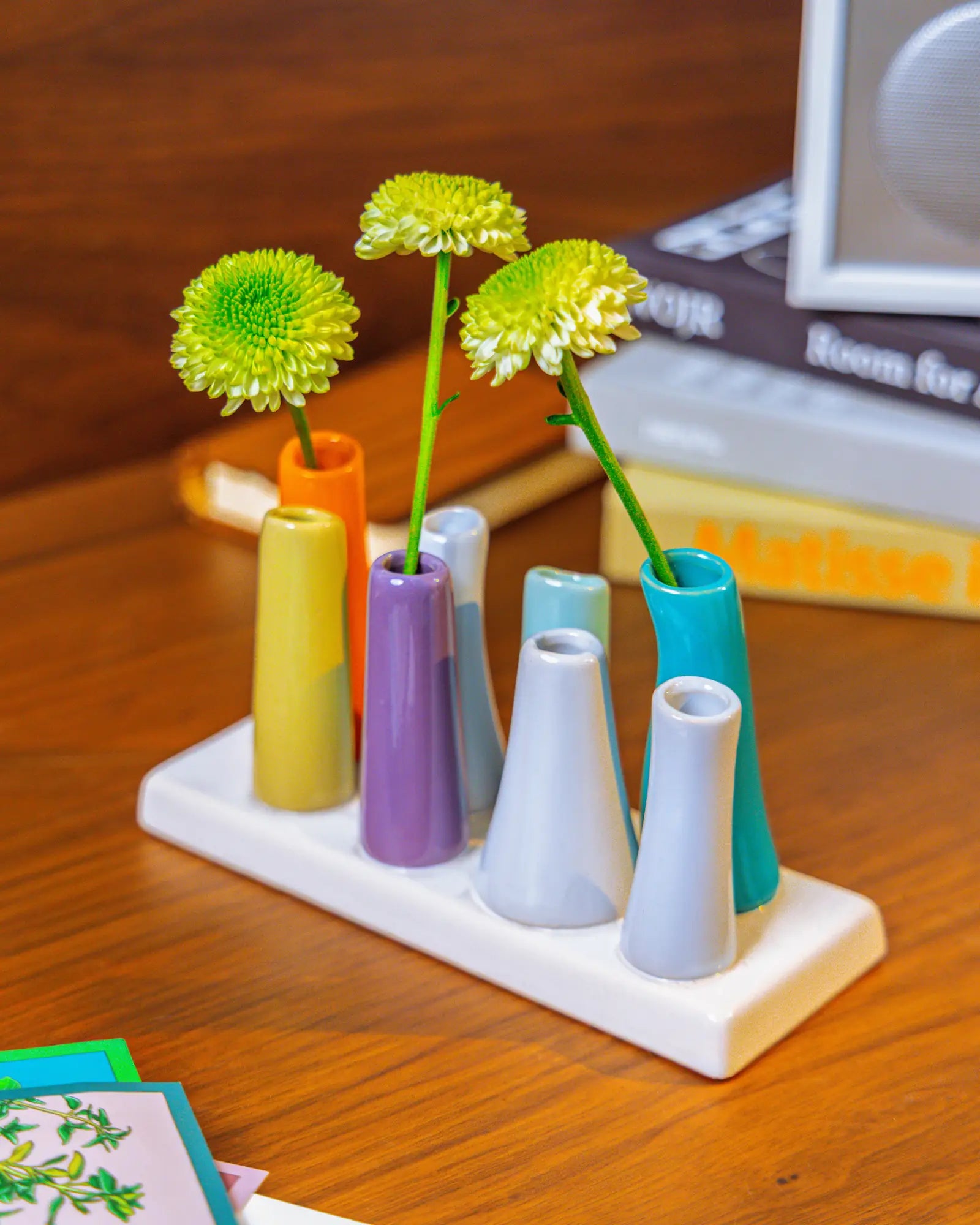 Chive ceramic pooley bud vase in color orange, styled with fresh flowers, on a wood desk.
