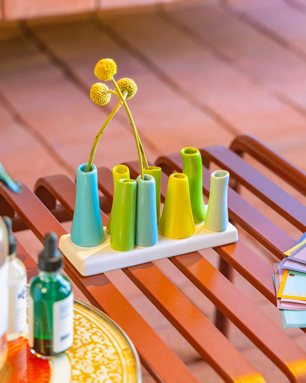 Chive ceramic pooley bud vase in color scout blue, styled with fresh flowers, on a red bench.