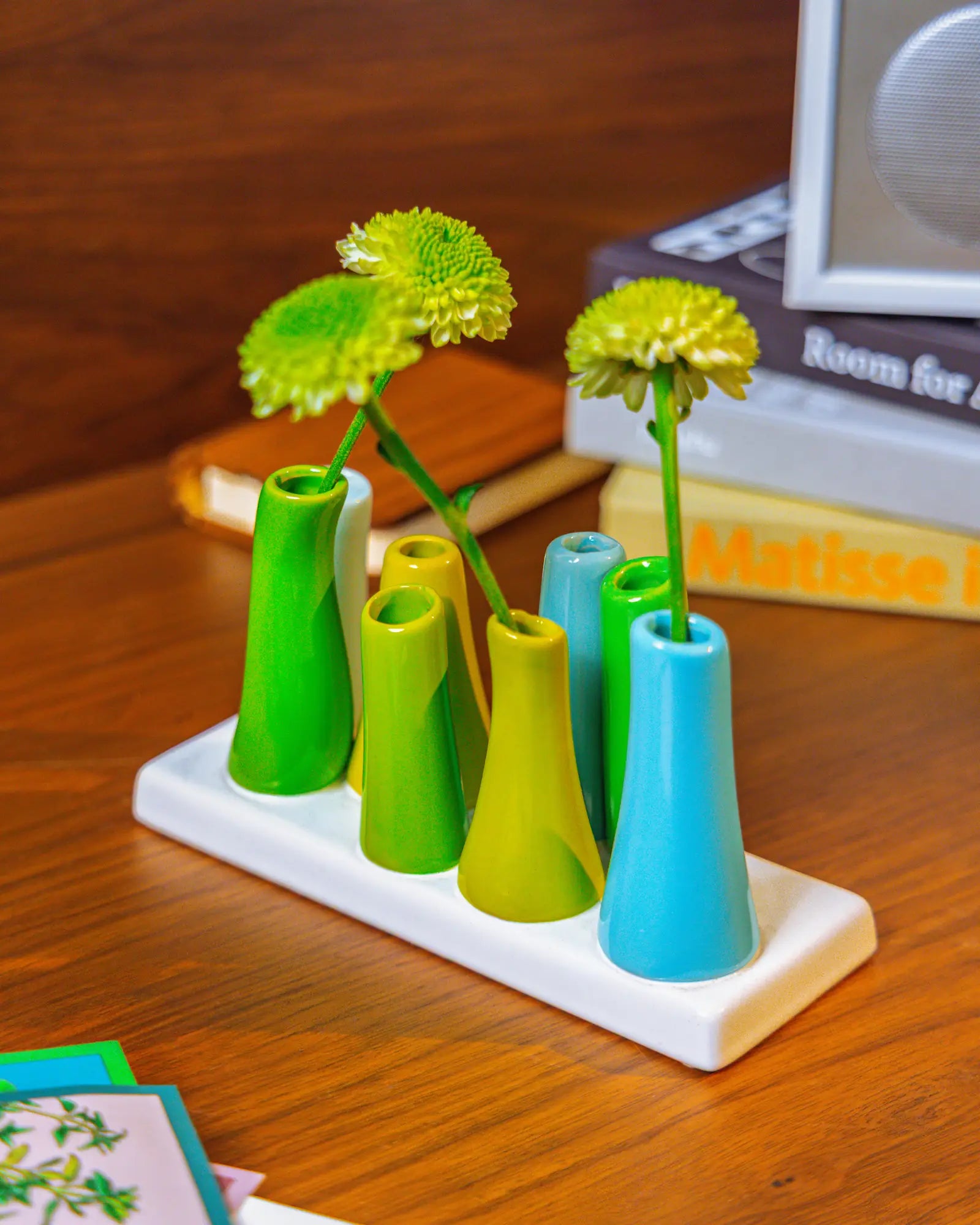 Chive ceramic pooley bud vase in color scout blue, styled with fresh flowers, on a wood desk.