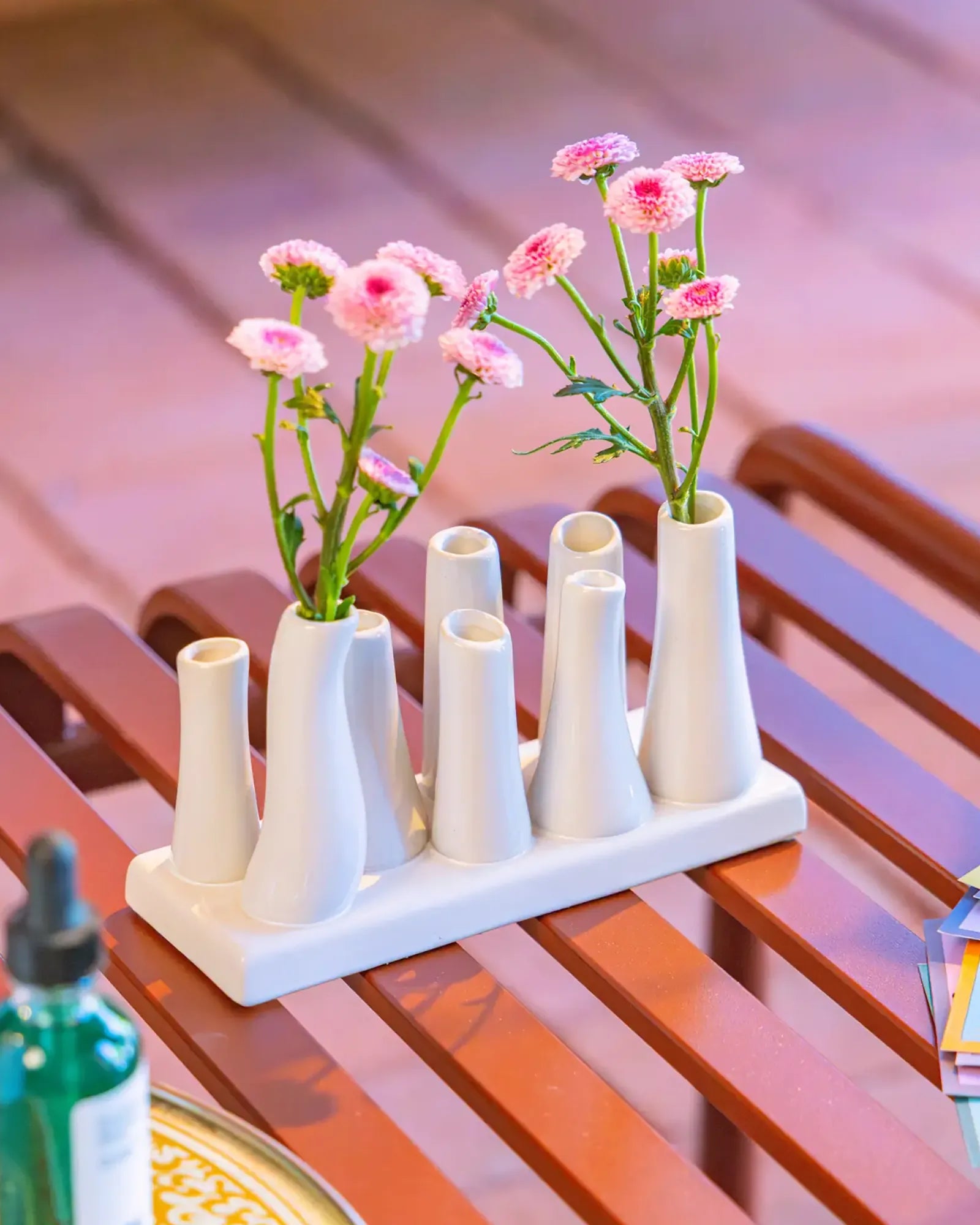 Chive ceramic pooley bud vase in white, styled with fresh pink flowers, on a red bench.