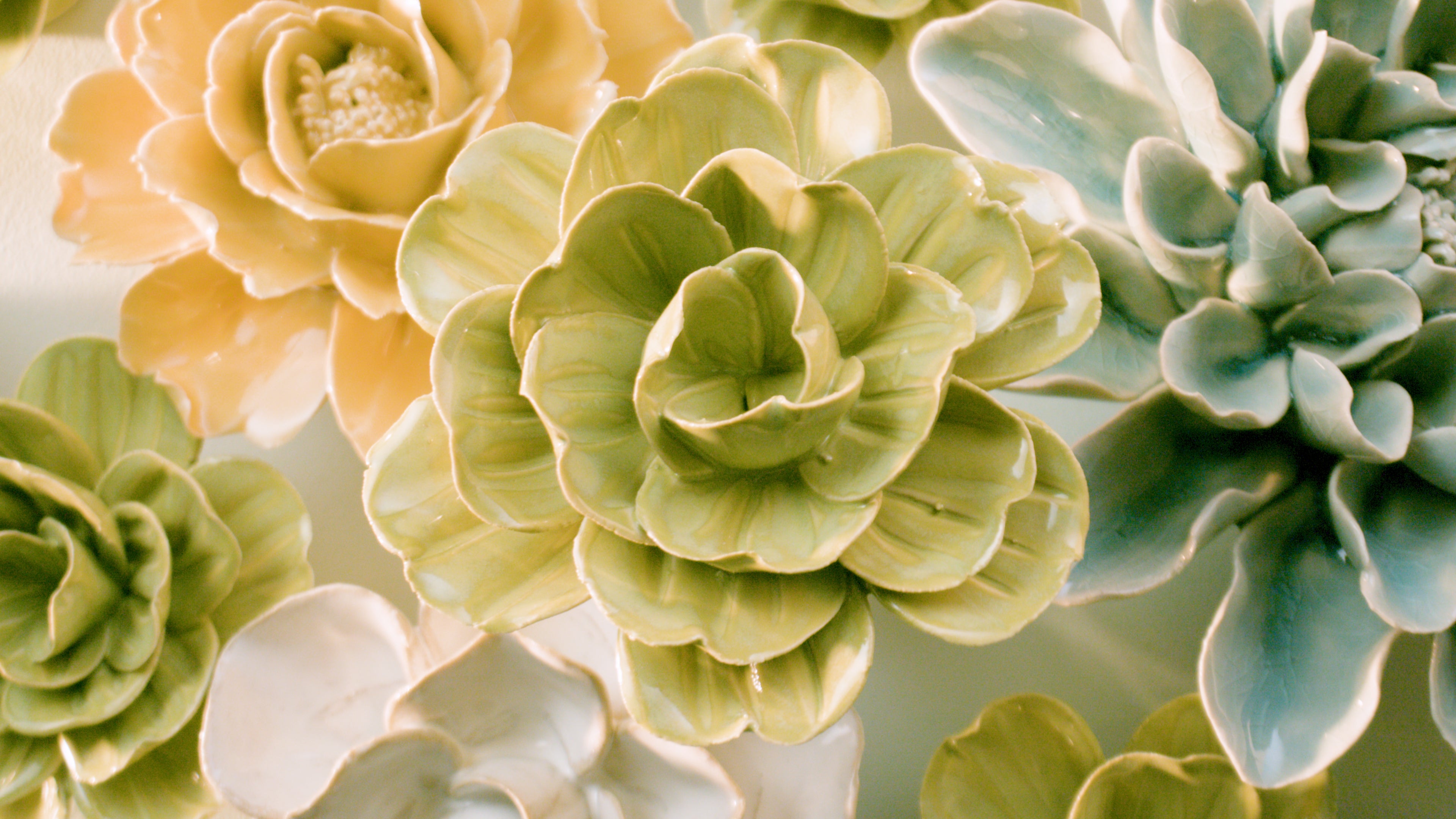 Macro pan across twenty hand-glazed ceramic wall flowers in five palettes — unique wall decor by Chive Studio