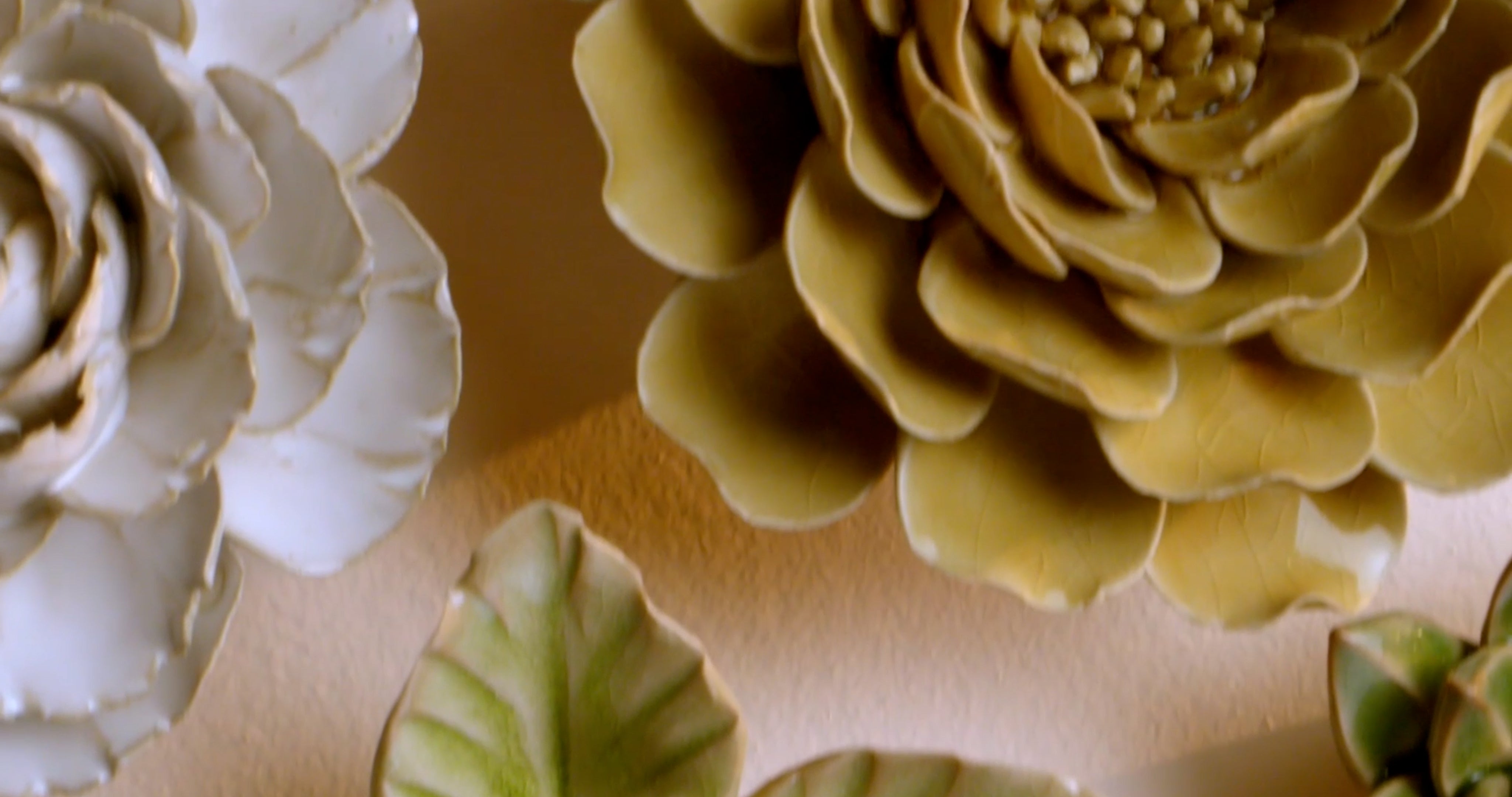 A macro pan across twenty hand-glazed ceramic wall flowers from five collections — unique wall decor that hangs on a single screw.